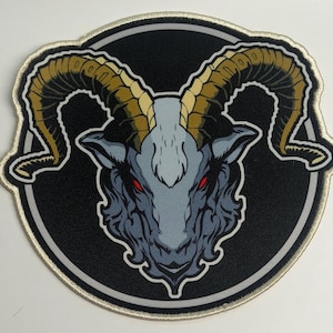 May include: Embroidered patch featuring a stylized ram's head. The ram's head is gray with red eyes and large, curved, tan horns. The patch is circular, with a black background and a silver and tan border.