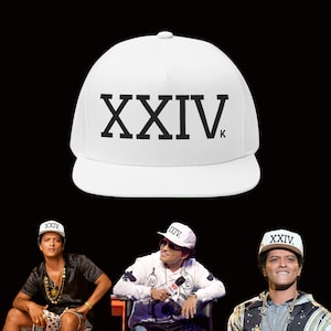 May include: White baseball cap featuring the text "XXIVK" in black. The cap has a flat peak and a rounded crown. The image also shows three people wearing the same cap.