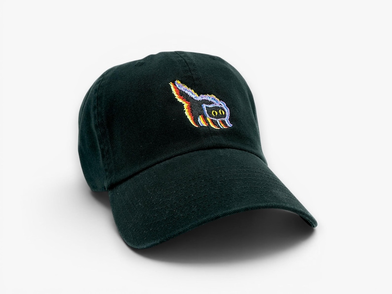 May include: A dark green baseball cap with a curved brim. The cap features a colorful embroidered design of a cartoon skunk on the front. The skunk has a rainbow-colored tail and a pair of eyes. The cap is made of a soft, durable fabric.