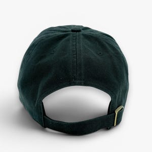 May include: Dark green baseball cap with a curved brim and adjustable strap. The cap is made of a soft fabric and features a metal buckle closure. The back of the cap is visible against a white background.
