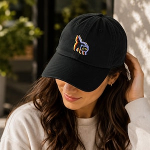 May include: Black baseball cap with a curved brim. The cap features a colorful embroidered design of a cat. The hat is made of a soft material and has an adjustable strap.
