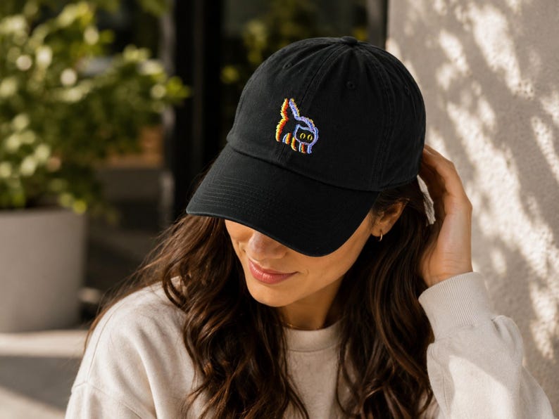May include: Black baseball cap with a curved brim. The cap features a colorful embroidered design of a cat. The hat is made of a soft material and has an adjustable strap.