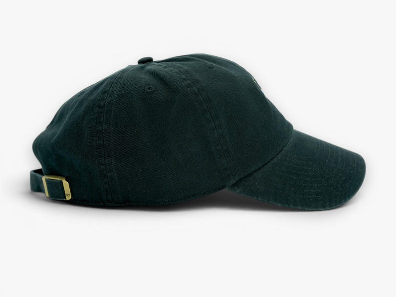 May include: A dark green baseball cap with a curved brim and adjustable strap. The cap has a metal buckle and a small button on top. The hat is made of a soft, textured fabric.