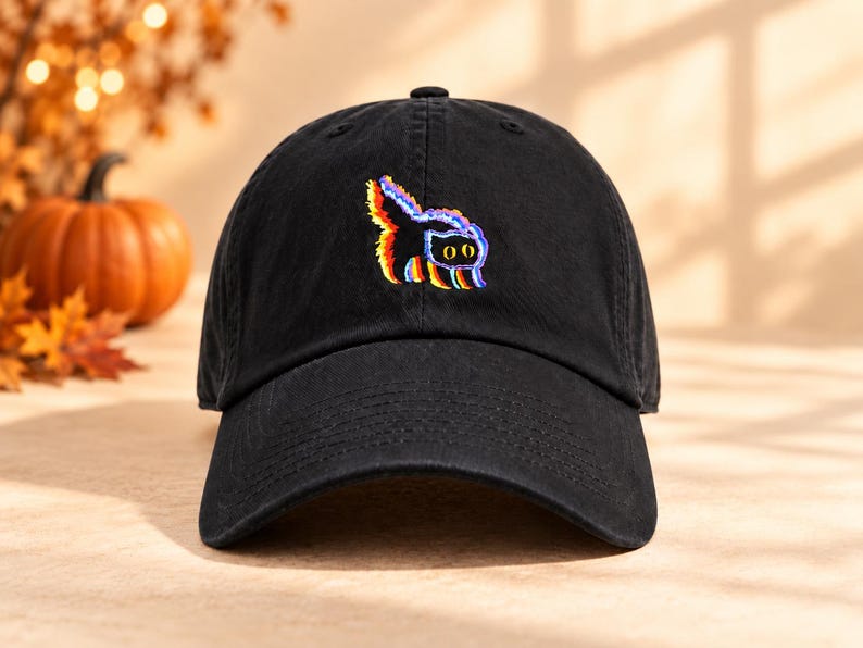 May include: A black baseball cap featuring an embroidered graphic of a cat with a glitch effect. The cat design incorporates vibrant red, yellow, and blue colors, creating a multi-layered visual appearance against the solid black fabric of the hat.