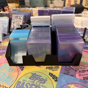 May include: A black card organizer filled with baseball cards in protective sleeves. The cards are arranged in rows within the organizer. The background features a colorful Topps Major League Baseball design.