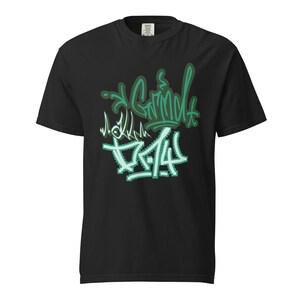 May include: Black t-shirt with a green and white graffiti design. The design includes the words "Grind" and "Truth" in a stylized font. The shirt is made of a soft material.