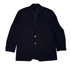 Puede incluir: Un blazer azul marino con botones dorados. El blazer tiene dos bolsillos delanteros y un bolsillo en el pecho. Las mangas tienen botones en los puños. Un estilo clásico.