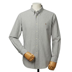 Puede incluir: Una camisa gris con botones y rayas blancas verticales. La camisa de manga larga tiene cuello abotonado y un pequeño logotipo bordado en el pecho. La camisa se exhibe en un maniquí.