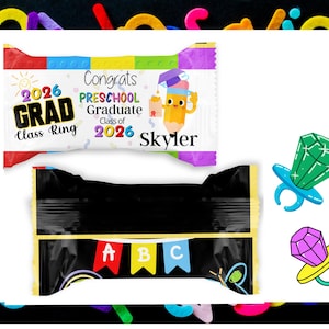 May include: Two candy wrappers with colorful designs. One wrapper reads "2026 GRAD Class Ring" and "Congrats PRESCHOOL Graduate Class of 2026 Skyler." The other wrapper has "ABC" on a banner. Also, two ring pop candies are shown.