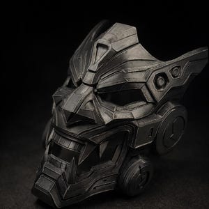May include: A black mask with a complex, geometric design. The mask has sharp angles, a pronounced brow, and a stylized mouth. The design suggests a futuristic or fantasy theme, with a dark colour scheme.