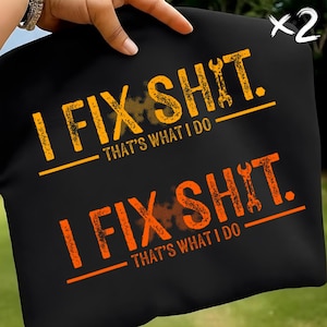 May include: Two black t-shirts with the text "I FIX SHIT. THAT'S WHAT I DO" in orange and yellow. The design includes a wrench graphic. The shirts are held up by a hand.