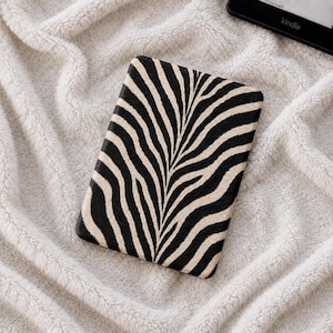 May include: A rectangular e-reader cover featuring a black and cream-colored zebra stripe pattern. The design displays a symmetrical arrangement of organic, flowing lines that mimic the natural appearance of animal fur across the entire surface.