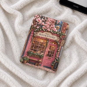 Peut inclure: Une housse de liseuse rectangulaire avec une illustration imprimée d'une devanture rose portant le mot BOOKSTORE au-dessus de la porte. Le motif comprend des fleurs roses, une vitrine remplie de livres et un panneau Books Coffee Good Vibes.