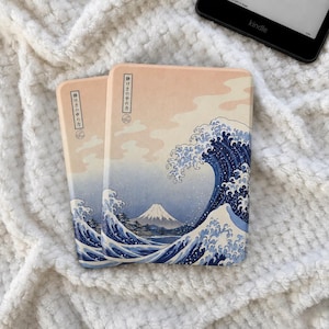 Pode incluir: Uma capa retangular para leitor de e-books com uma estampa gráfica de uma grande onda azul e um pico de montanha contra um céu pêssego pálido. O design inclui texto japonês vertical em uma caixa branca no lado esquerdo da capa.