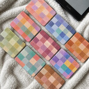 Könnte beinhalten: Eine Sammlung von neun rechteckigen Karten mit einem Raster aus farbigen Quadraten in verschiedenen Paletten, darunter Orange-, Rosa-, Blau-, Grün- und Brauntöne. Jede Karte zeigt ein einzigartiges Schachbrettmuster mit weichen, texturierten Farbblöcken.