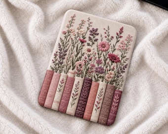 May include: A rectangular e-reader cover featuring an embroidered design of vertical book spines in shades of pink, mauve, and burgundy, topped with a dense arrangement of wildflowers in pink, purple, and white thread on a cream-coloured fabric.