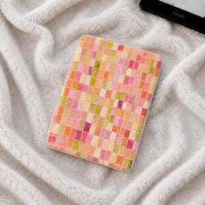 Peut inclure: Un étui rectangulaire pour liseuse électronique présentant un motif mosaïque vibrant composé de petits carrés dessinés à la main dans des tons de rose, orange, jaune et vert clair. La surface présente un quadrillage de tuiles variées.