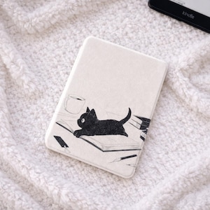 Puede incluir: Una funda rectangular para lector electrónico con fondo color crema que presenta un dibujo lineal negro de un gato acostado sobre un libro abierto junto a una taza y un bolígrafo. El diseño incluye una pequeña pila de libros y un marcapáginas.