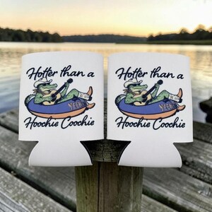 K&ouml;nnte beinhalten: Zwei wei&szlig;e Dosenk&uuml;hler aus Schaumstoff mit einer Grafik eines gr&uuml;nen Alligators, der einen Cowboyhut und Stiefel tr&auml;gt und in einem blauen Schwimmreifen Gitarre spielt. Der Text lautet Hotter than a Hoochie Coochie in schwarzer Schrift.