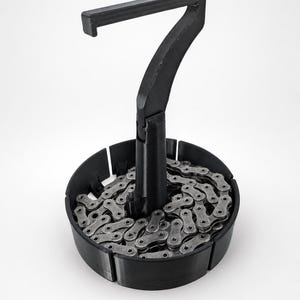May include: A black plastic stand shaped like the number seven, featuring a circular base filled with a coiled metallic bicycle chain. The structure has a vertical post rising from the center of the base, topped with a horizontal arm.
