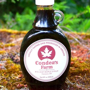 Peut inclure: Une bouteille en verre foncé de sirop d'érable Big Leaf de Condea's Farm. L'étiquette présente une feuille d'érable rouge et le texte "Locally Tapped and Produced in Oregon." La bouteille contient 236 ml de sirop et possède une anse.