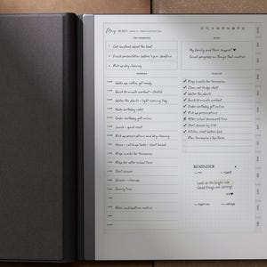 K&ouml;nnte beinhalten: Ein schwarzer E-Reader mit ge&ouml;ffnetem digitalem Planer, der einen Tagesplan und eine To-Do-Liste anzeigt. Der Bildschirm zeigt handschriftliche Notizen und einen Erinnerungsbereich. Das Ger&auml;t liegt auf einer braunen Oberfl&auml;che.