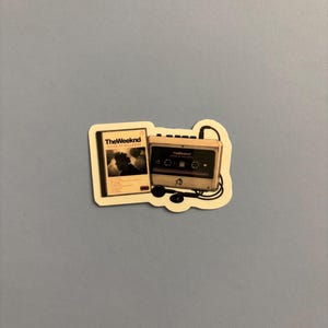 Puede incluir: Una pegatina troquelada que muestra un casete y la portada del álbum House of Balloons de The Weeknd. El casete es de color beige con detalles en negro, el logotipo XO y auriculares con cable negros. La portada del álbum es blanca con texto negro.