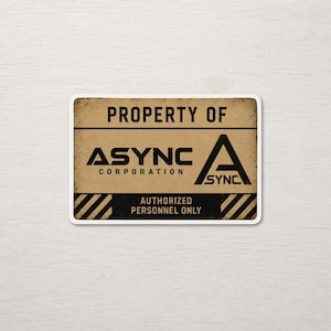 May include: A rectangular sticker with a distressed tan background and black text. It reads PROPERTY OF ASYNC CORPORATION with a large A logo. The bottom section features black and tan diagonal hazard stripes and the text AUTHORIZED PERSONNEL ONLY.