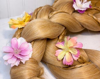 May include: A long, braided wig in a light golden-brown color, adorned with colorful artificial flowers. The braid is thick and detailed, with a net securing the base. The flowers are pink, yellow, and white.