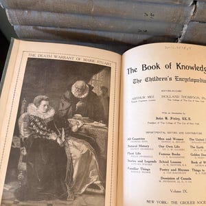 以下が含まれることがあります： 「The Book of Knowledge」というタイトルの開いた本と、メアリー・スチュアートのイラスト。この本は百科事典のコレクションの一部です。本の表紙は色あせた青色です。