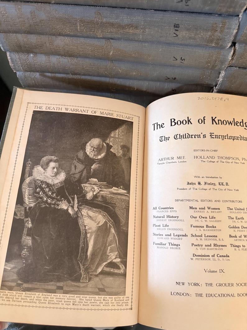 以下が含まれることがあります： 「The Book of Knowledge」というタイトルの開いた本と、メアリー・スチュアートのイラスト。この本は百科事典のコレクションの一部です。本の表紙は色あせた青色です。