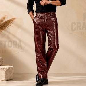 May include: Deep burgundy trousers featuring a glossy crocodile skin texture. These trousers have a structured waistband with a single button closure, belt loops, and a straight-leg cut. The material has a reflective finish and a distinct reptilian pattern.