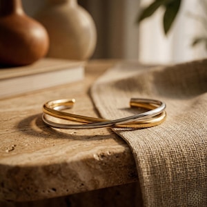 Könnte beinhalten: Ein Set aus drei Keramikbechern mit gesprenkelter, matter Oberfläche. Die Becher sind in Creme-, Hellgrau- und Dunkelgrautönen gehalten. Jeder Becher hat ein schlichtes, minimalistisches Design.