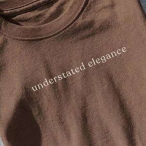 May include: A white ceramic mug with a black handle and the text "But First, Coffee" in a black, bold font. The mug is on a wooden surface. The mug is 10 cm tall.