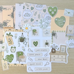 May include: A collection of stationery items including stickers and paper sheets featuring illustrations of teapots, daisies, hearts, and furniture. Text on the items includes "take your time," "just breathe," "some peace," "slow down," "quiet mind," and "a little pause."