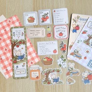 May include: A collection of stationery items featuring apple-themed illustrations and mice characters. Includes a red gingham patterned paper, a bookmark, a guest list, sticker sheets, and small die-cut labels with text like Fresh Picked Apples.