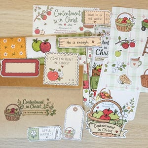 May include: A collection of paper stationery items featuring apple-themed illustrations and the text Contentment in Christ. Includes a brown envelope, sticker sheets with baskets, wagons, and ladders, die-cut labels, and tags with floral accents.