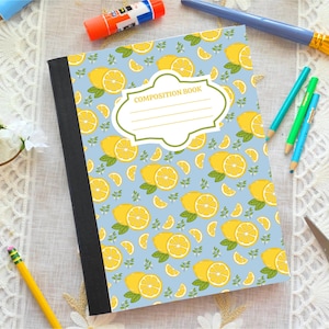 May include: A composition book with a light blue cover featuring a repeating pattern of yellow lemon slices and green leaves. The center has a white label with a decorative green border and the text COMPOSITION BOOK with four blank lines.