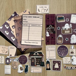 May include: A collection of stationery items featuring a Little Ghost Bookshop theme, including stickers, bookmarks, and library checkout cards. The designs incorporate ghosts, books, a bookstore building, and text such as "Lost in a good book" and "Little Ghost Bookshop" in shades of purple, brown, and cream.