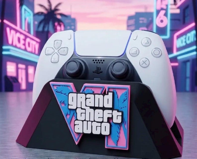 Puede incluir: Un mando de videojuegos blanco y negro descansa sobre un soporte negro con una placa gr&aacute;fica rosa y azul con el texto Grand Theft Auto VI. El mando tiene botones est&aacute;ndar, dos joysticks anal&oacute;gicos y un panel t&aacute;ctil central claramente visibles.