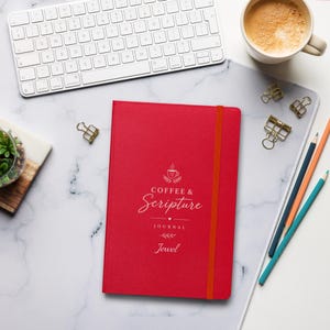 May include: A bright red journal with an orange elastic band closure. The cover features white text that reads Coffee & Scripture JOURNAL and the name Jewel, accompanied by a small coffee cup icon and decorative flourishes.