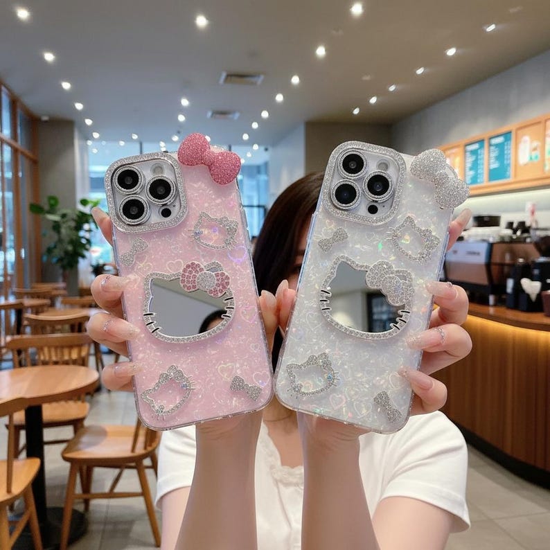 Puede incluir: Dos fundas decorativas para tel&eacute;fono, una rosa y otra blanca, con un dise&ntilde;o de Hello Kitty. Cada funda tiene un lazo en la parte superior y est&aacute; adornada con pedrer&iacute;a. Las fundas tienen un espejo en el centro.