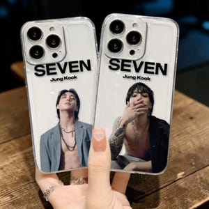 May include: Two clear phone cases, each displaying the word "SEVEN" and "Jung Kook". The cases feature images of a person. One image shows a person in a grey blazer, the other a person with tattoos. The cases are held by a hand.