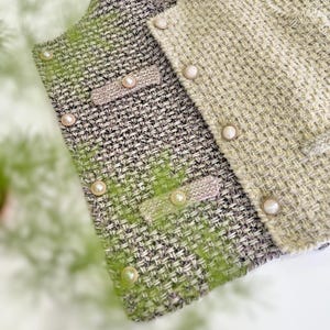 May include: Close-up of two tweed jackets. One is a mix of gray, green, and white, with pearl-like buttons and a decorative pocket detail. The other jacket is a light green color with similar pearl buttons. The jackets are likely part of a clothing collection.