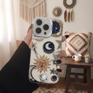 May include: Clear phone case with celestial-themed embellishments. Features a sun, moon, and stars design with beaded and rhinestone accents. The case has a silver camera frame and the text "SO COOL".