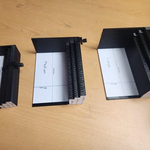 Può includere: Tre staffe nere a forma di L etichettate Small, Medium e Large. Ogni staffa presenta una base bianca con misure stampate in millimetri, tra cui 50mm, 90mm, 135mm e 160mm. Le staffe hanno un bordo verticale testurizzato e una piccola manopola.