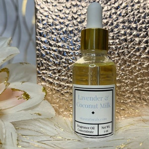 May include: A clear glass bottle with a gold lid and dropper. The bottle contains a light yellow liquid. The label is white with black text that reads "Lavender & Coconut Milk" and "oilnaturals.com". The label also says "Fragrance Oil Concentrate" and "Net Wt. 1 oz".