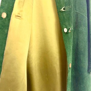 May include: A green suede coat with a light yellow lining. The coat has a button closure and decorative gold-colored clasps. The coat is open, revealing the interior lining.