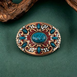 May include: An oval-shaped, copper-colored belt buckle with a turquoise center stone. The buckle is adorned with turquoise, red, and white accents. The design features an ornate, filigree pattern, creating a vintage, western aesthetic.