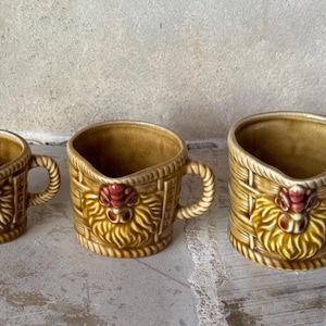 May include: A white ceramic mug with a black handle and the text "But First, Coffee" in a black, handwritten-style font. The mug is on a white surface.